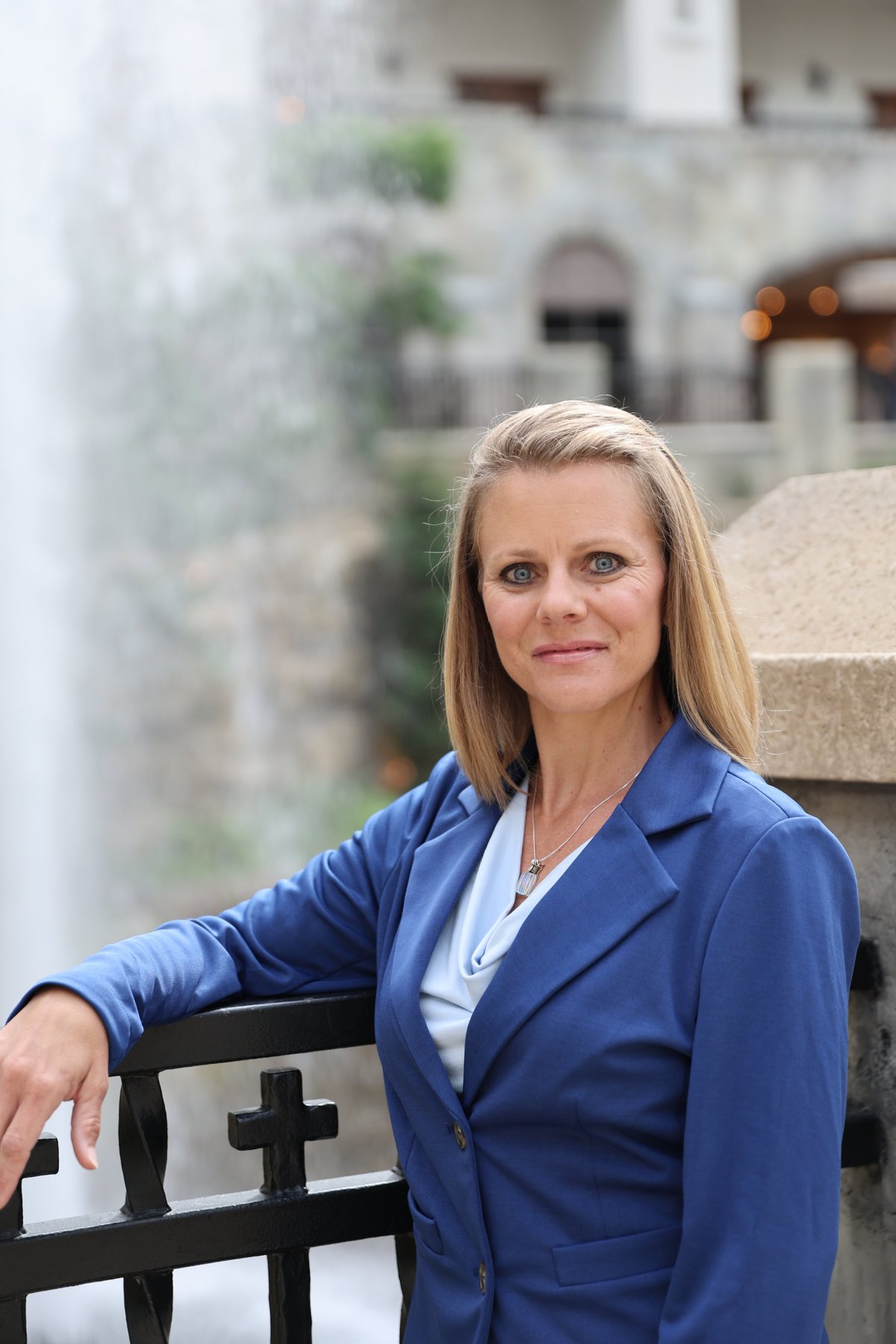 Professional portrait of a woman in a blue blazer posing against an old stone building